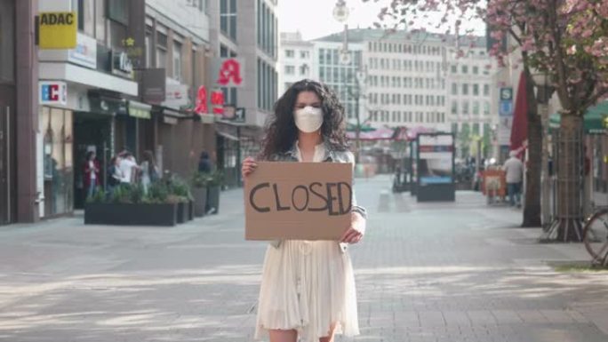 德国法兰克福，2020年4月8日年轻女性在购物街上抱着防电晕病毒的防护口罩，举着封闭的牌子
