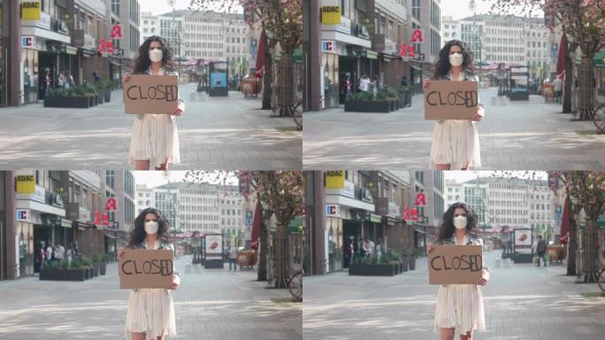 德国法兰克福，2020年4月8日年轻女性在购物街上抱着防电晕病毒的防护口罩，举着封闭的牌子