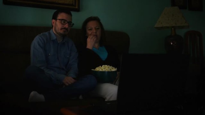 一个年轻人和他的母亲在客厅的笔记本电脑上看电影