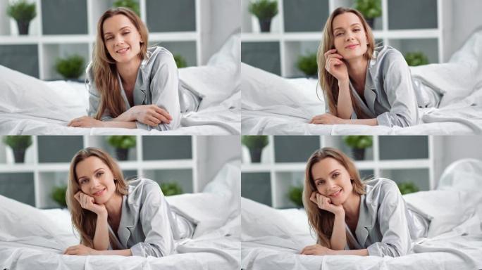 穿着睡衣在床上摆姿势的微笑的国内早晨年轻女子的肖像。4k龙红相机