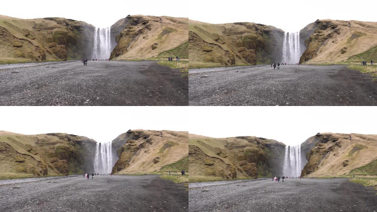冰岛南部的Skogafoss瀑布，在金环上。游人前来看瀑布，游人在山脚下散步。