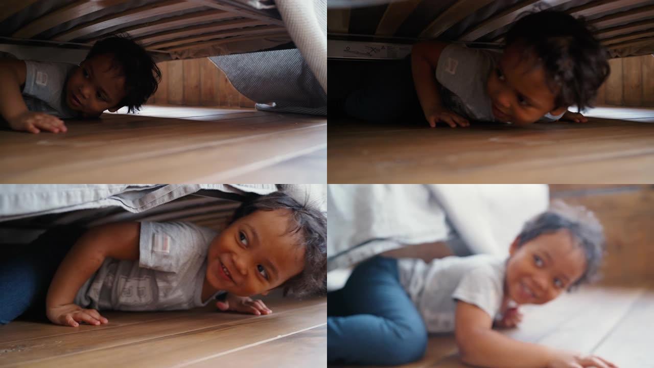 隐藏的婴儿躺在床上笑着爬出。孩子在床下找东西。