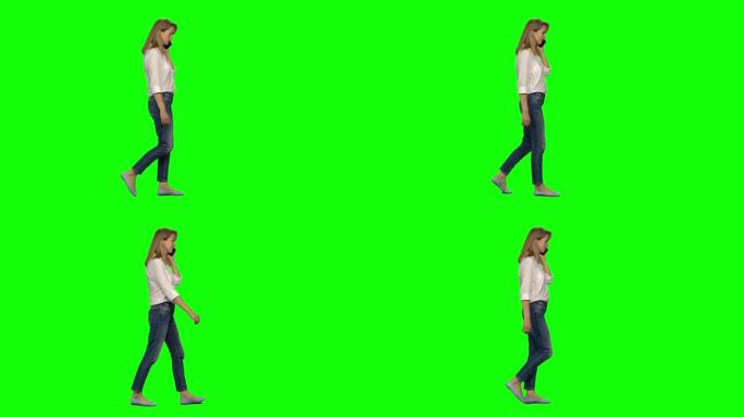 金发女子在绿屏上平静地在手机上行走和交谈。色度键，4k镜头。纵断面视图
