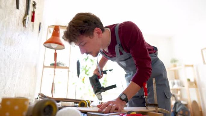 年轻的男工匠在滑板板上钻孔