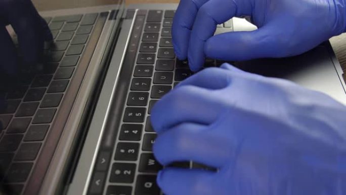 医生的手戴着蓝色手术手套在笔记本电脑键盘上打字