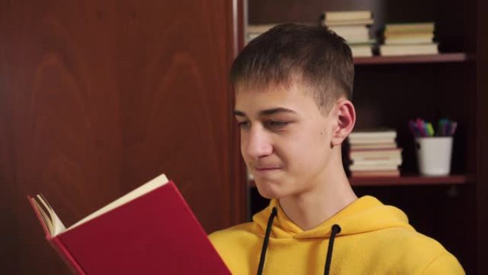 在家中的年轻学生在装有教科书的书柜的背景上看书