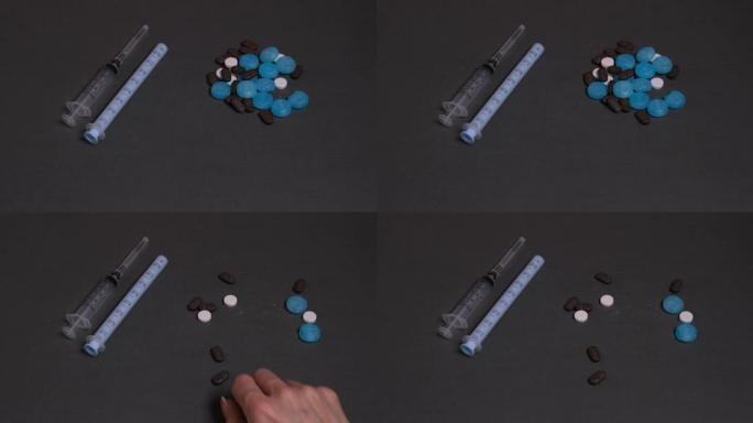 女性的手在灰色的背景上服用多种颜色的药丸。在灰色的背景上有暗淡的注射器，药丸。药物和毒瘾的概念