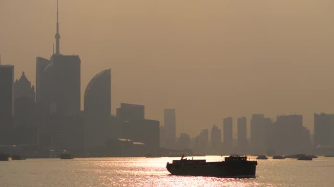 在黄浦江上航行的货船剪影，黄昏时以上海外滩天际线为背景，4k镜头，b滚动镜头。