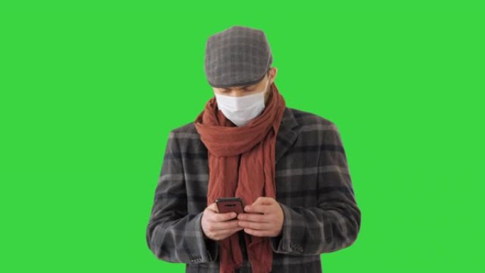 戴着医用口罩的绅士使用电话并在绿色屏幕上行走，色度键