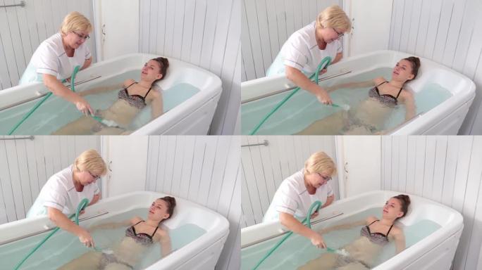 穿着泳衣的女孩躺在装有矿泉水的浴缸里。护士正在做按摩。