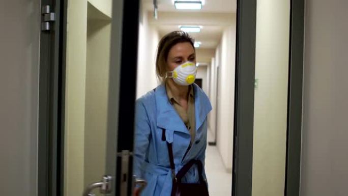 穿着蓝色斗篷和冠状病毒新型冠状病毒肺炎的防护面具的美女进入她的房子的入口，并用钥匙打开门。在流行病期