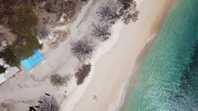 一对夫妇躺在印度尼西亚龙目岛粉红海滩海滨的沙滩上玩无人机。波浪轻轻地冲刷着海岸。他们在晒黑。快乐和粗