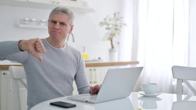沮丧的高级老人用笔记本电脑做大拇指