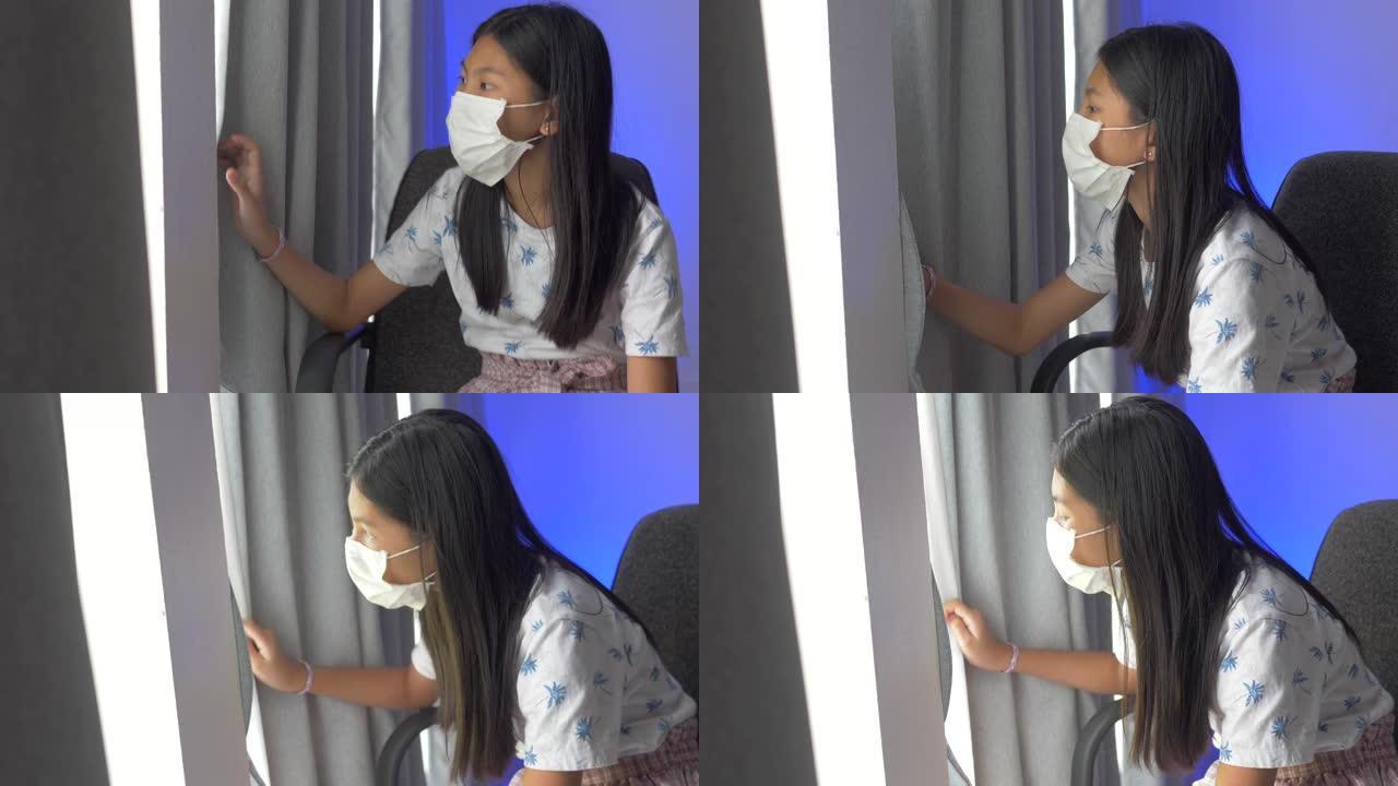 新型冠状病毒肺炎期间，戴着面具的亚洲女孩看着窗外。