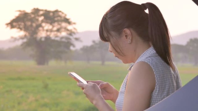 亚洲妇女坐在车后，在日落国家公园的社交梅达使用智能手机，背景山