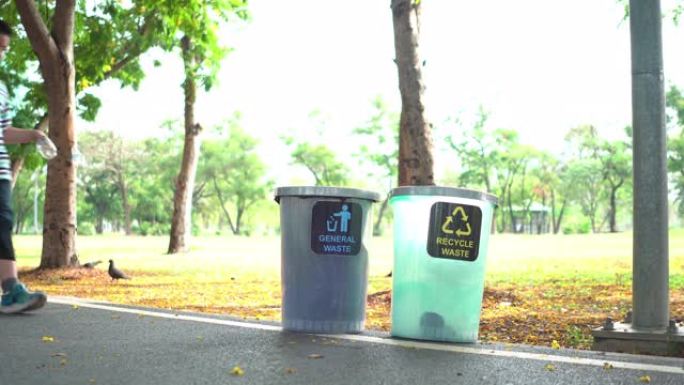 侧视图: 周末阳光明媚的日子，亚洲家庭，母亲，兄弟和姐妹在公园的回收站中步行并分离透明塑料瓶作为回收