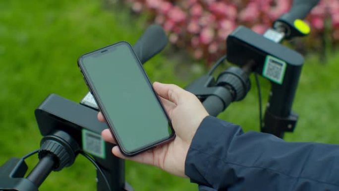 年轻人为电动踏板车付费使用带有绿色模拟屏幕智能手机的应用程序。绿屏智能手机。