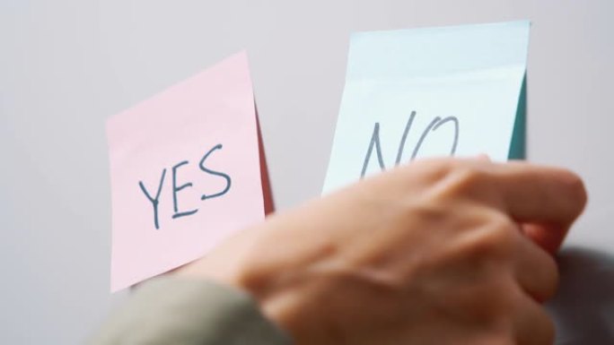 一只女性的手撕下蓝色贴纸的特写镜头，上面写着 “否”，在灰色板上留下粉红色的贴纸。选择的概念