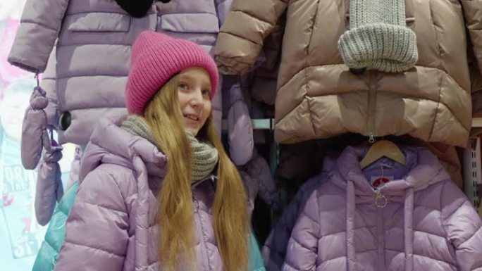 十几岁的女孩在购物时在服装店尝试羽绒服。快乐的年轻女孩在购物商店展示新的羽绒服。青年在陈列室购物。
