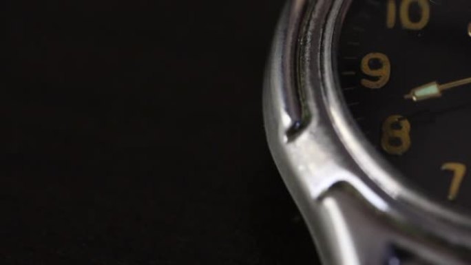 桌子上有一只手表。表盘的一部分是可见的。秒针移动。拍摄特写，在黑色背景上