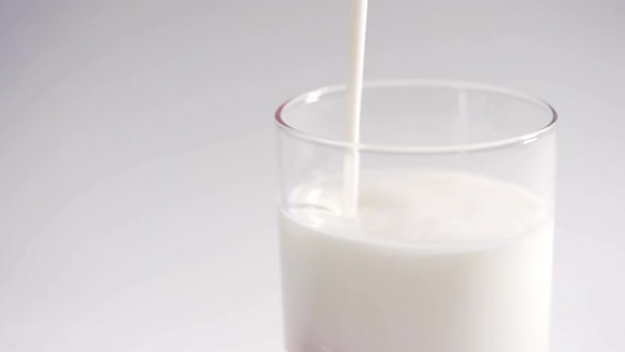 一个人将新鲜的有机酸奶倒入透明玻璃杯中。牛奶酸奶慢慢装满玻璃杯，在白色背景上隔离4k