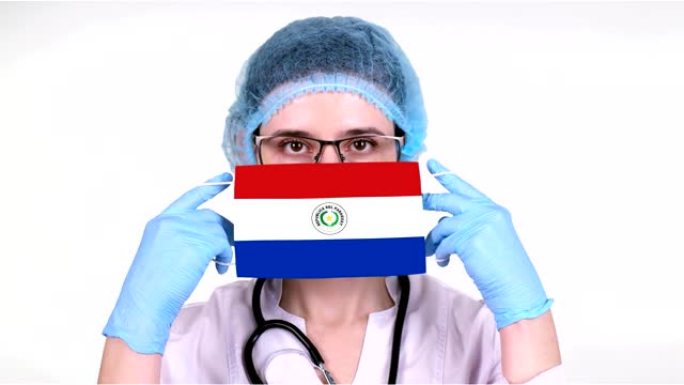 特写。戴眼镜的医生，蓝色医疗帽，手套手持带有巴拉圭国旗的医用口罩。医生护理，冠状病毒期间国家保护，全