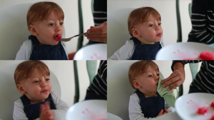 一岁婴儿吃甜点，婴儿拍手。母亲用餐巾纸擦拭幼儿的嘴