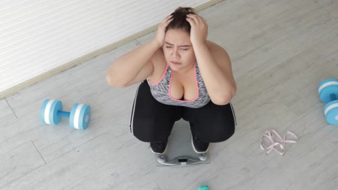 胖女人在健身室称重体重秤后做压力大的手势。加大码胖成熟女人或概念