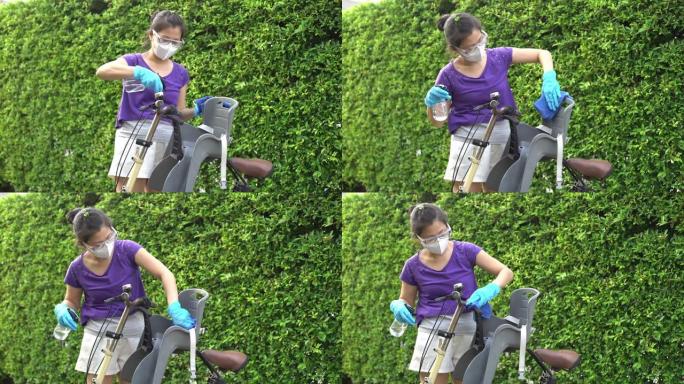亚洲母亲的双手戴着手套，以保持良好的卫生习惯，并在户外擦拭婴儿自行车座椅上的表面。