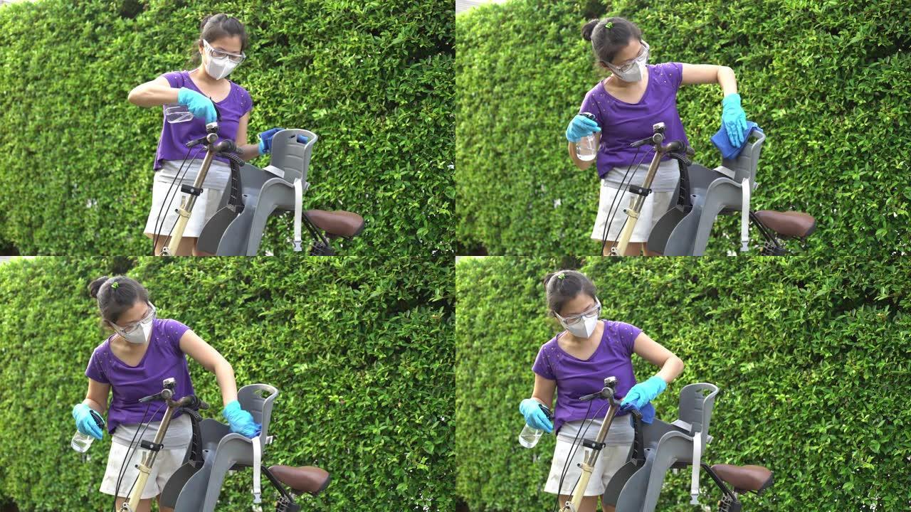 亚洲母亲的双手戴着手套，以保持良好的卫生习惯，并在户外擦拭婴儿自行车座椅上的表面。