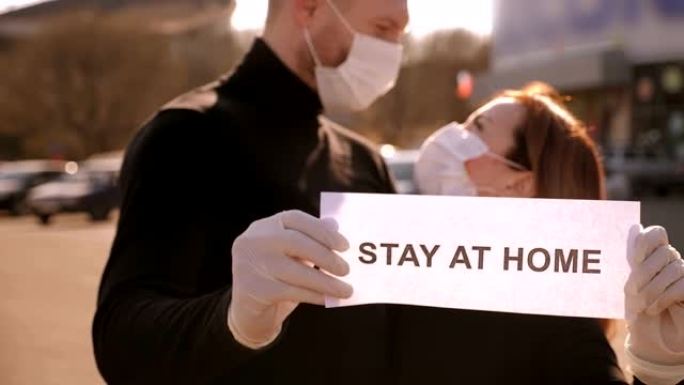 一对戴着医用口罩的夫妇拿着牌子呆在城市街道上的家里。