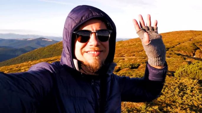 旅行博客作者穿着温暖在山顶上拍摄一个故事。年轻人手里拿着相机，可以看到山顶的景色。乌克兰喀尔巴阡山脉