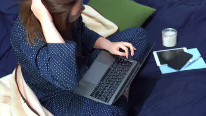 穿着经典蓝色睡衣的4K VDO亚洲女性使用电脑网络支持在家工作，保护电晕或新型冠状病毒肺炎病毒