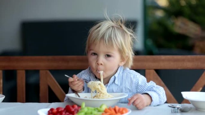 可爱的孩子，蹒跚学步的金发男孩，在花园夏天吃意大利面