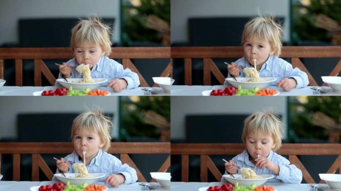可爱的孩子，蹒跚学步的金发男孩，在花园夏天吃意大利面