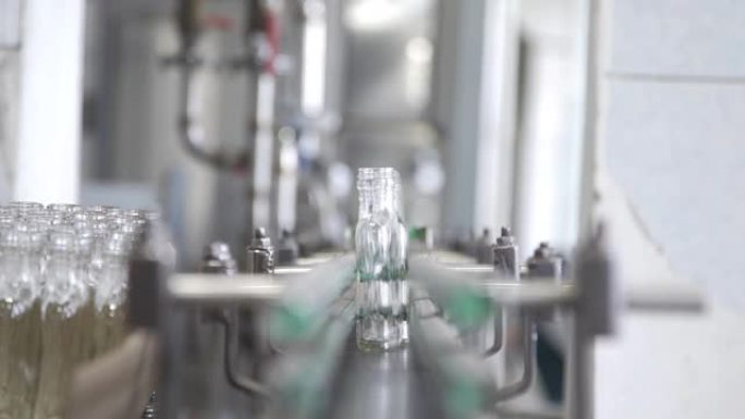 工人将空玻璃瓶放在酿酒厂生产线的传送带中，以装瓶伏特加酒。带有多条输送线的工作机，用于生产酒精饮料。