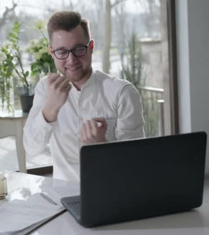 快乐商人的肖像，年轻成功的男人在笔记本电脑屏幕上看到了好消息，然后兴高采烈地跳舞，坐在白色办公室的桌