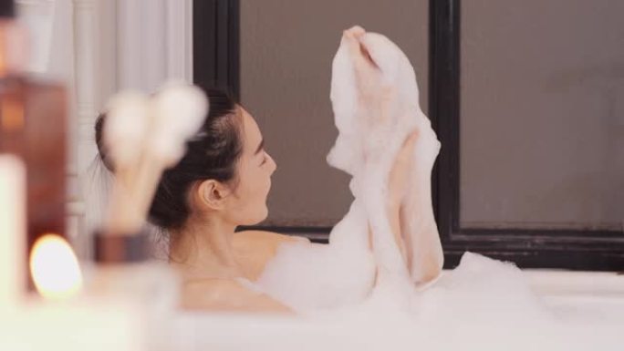 美丽的亚洲女人在浴室泡泡浴。她用快乐的情绪打扫自己。