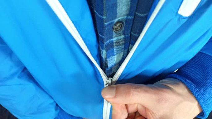 男人穿着时髦的带拉链的蓝色夹克。年轻人正在拉链夹克。寒冷天气概念。冬天来了。