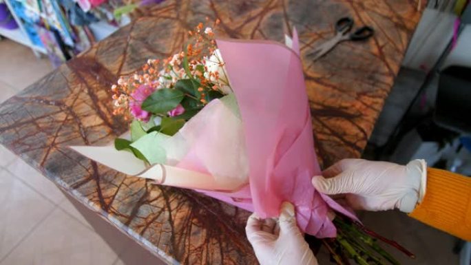 穿着乳胶手套的花店用粉色箔纸包裹花束