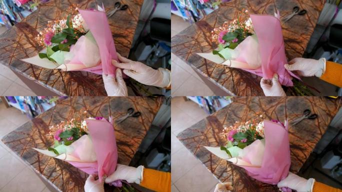穿着乳胶手套的花店用粉色箔纸包裹花束