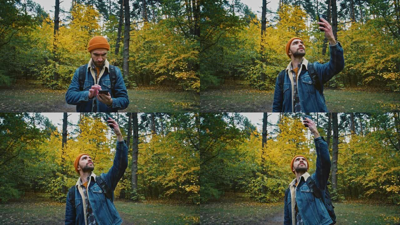 男子旅行者试图在电话上捕捉手机信号，独自行走在秋天的森林中，在手机上没有信号