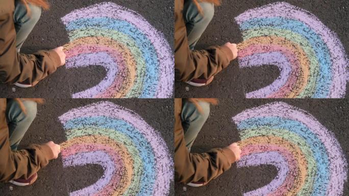 小女孩在沥青上画彩虹。孩子在街上画彩虹