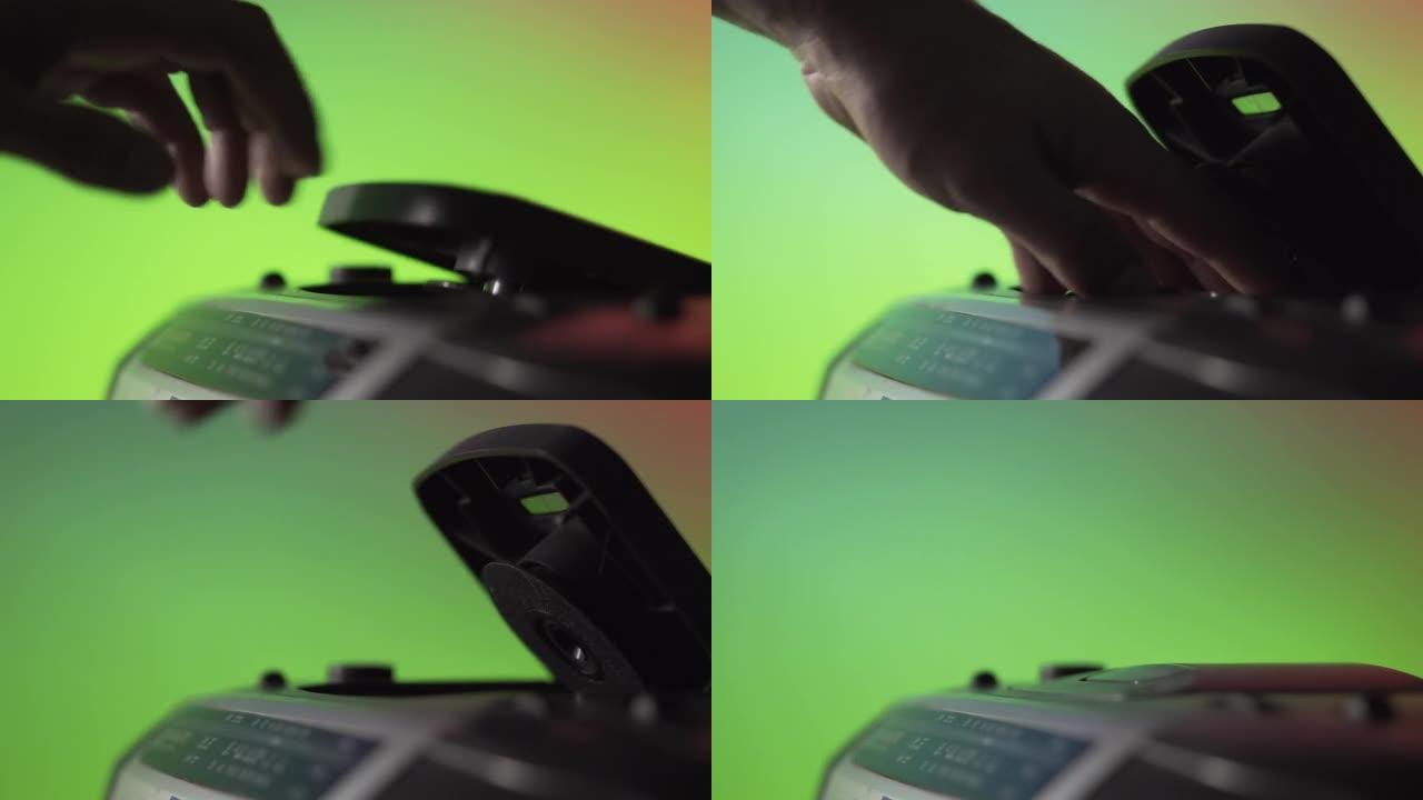 一名男子从绿色背景上的旧音乐播放器中取出激光CD光盘。手靠近。复古技术。上一代音频系统