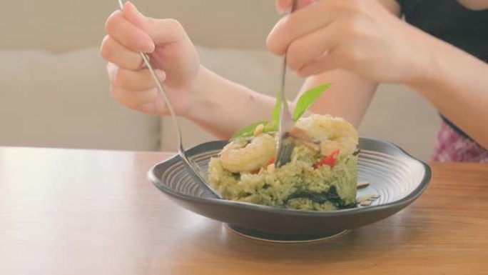 女人的手用叉子和勺子在木桌上白板上吃虾香蒜米饭。享受饮食理念。