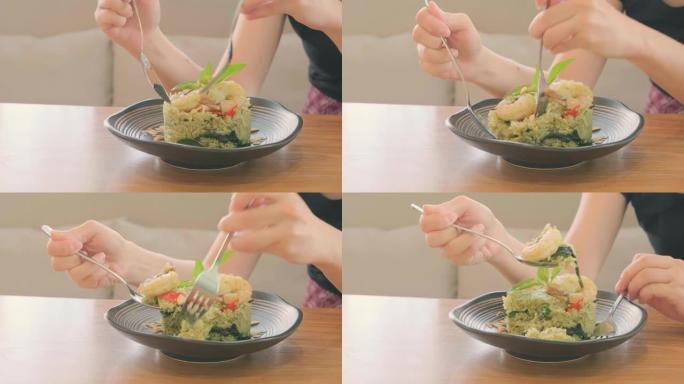 女人的手用叉子和勺子在木桌上白板上吃虾香蒜米饭。享受饮食理念。
