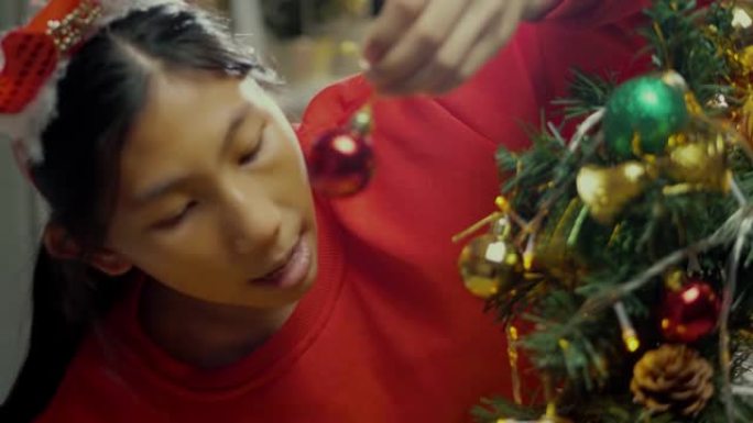 快乐的亚洲男孩穿着红色毛衣和发带装饰圣诞树，晚上在家，假期概念。