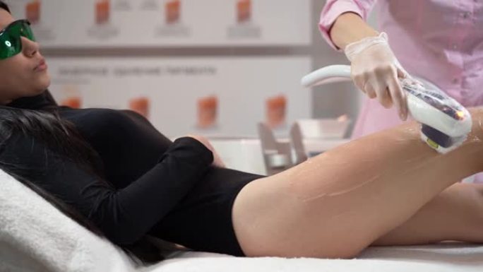 女美容师做激光脱毛苗条的腿美丽性感的女人是躺在美容沙龙的医疗沙发上。宇宙学，脱毛和水疗概念。身体保健