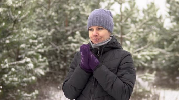 一个女孩在下雪天站在森林或公园里。游客很冷，擦着手咳嗽。