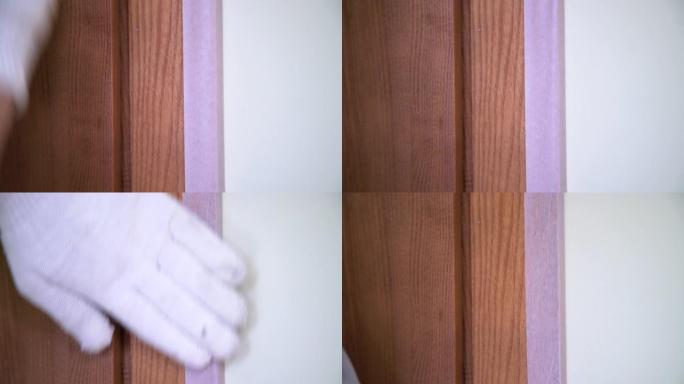 工人用手套在木门周围贴上保护胶带的特写-油漆准备室